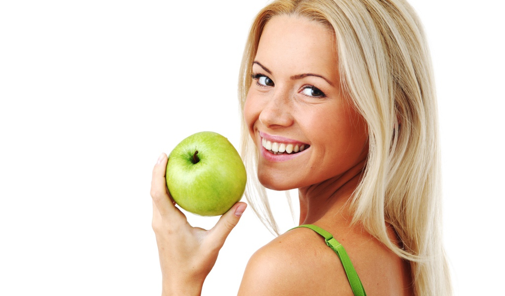 Улыбающаяся девушка блондинка с зеленым яблоком в руке на белом фоне