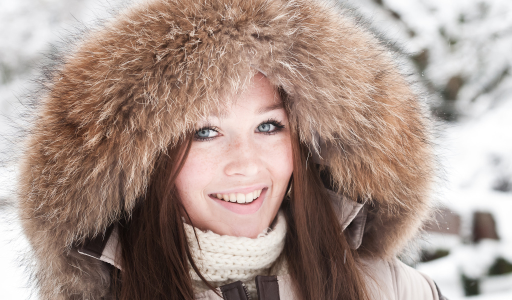 Улыбающаяся голубоглазая девушка в капюшоне зимой