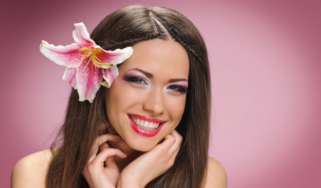 Улыбающаяся девушка с цветком лилии в волосах на розовом фоне 