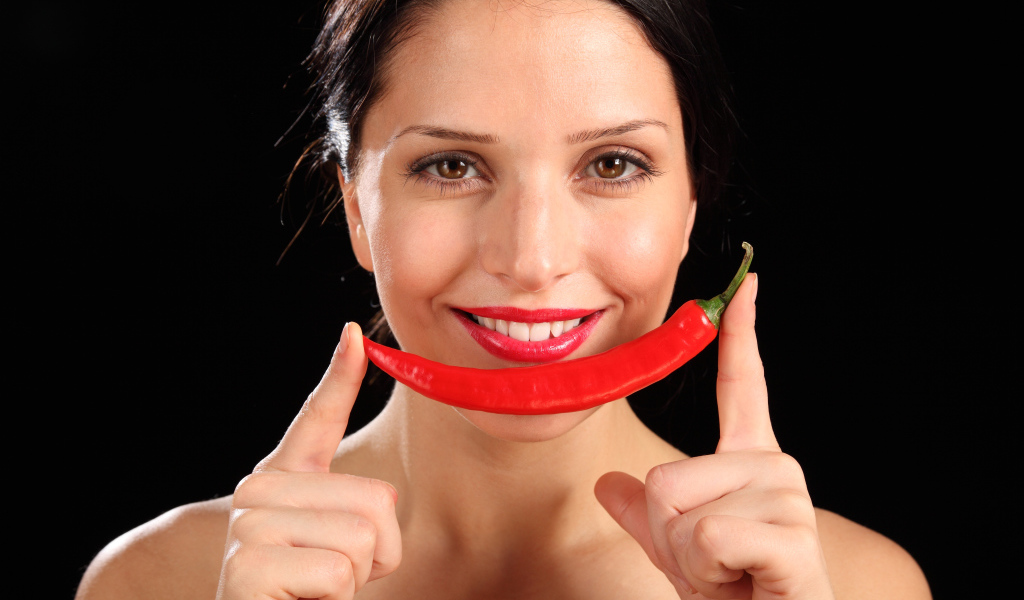 Улыбающаяся девушка с красным перцем на черном фоне