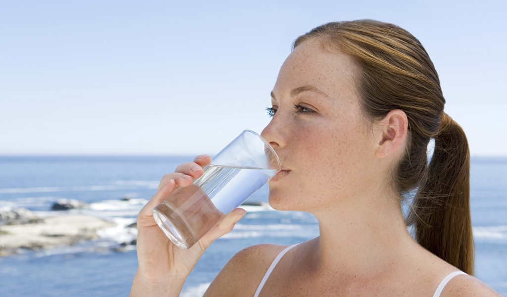 Девушка пьет воду со стакана на фоне моря