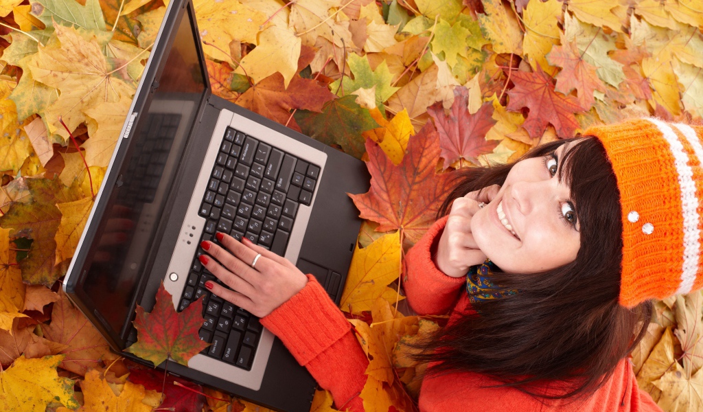 Девушка лежит на сухой опавшей листве с ноутбуком осенью