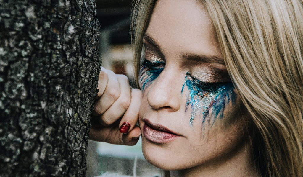 Заплаканная блондинка стоит у дерева