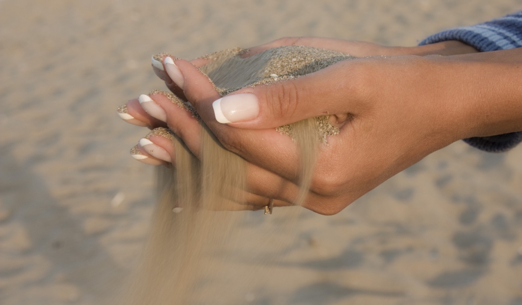Желтый песок в руках у девушки с красивым маникюром
