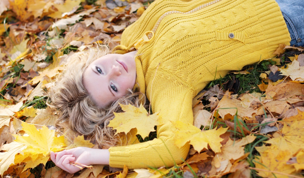 Молодая блондинка лежит на сухой листве осенью