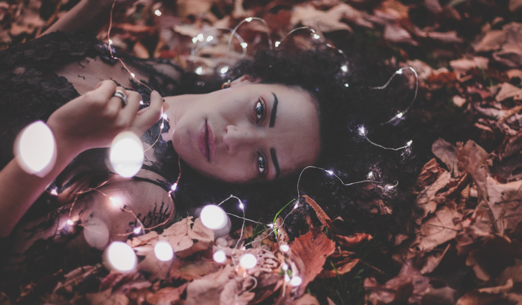 Молодая девушка лежит с гирляндой на желтых листьях