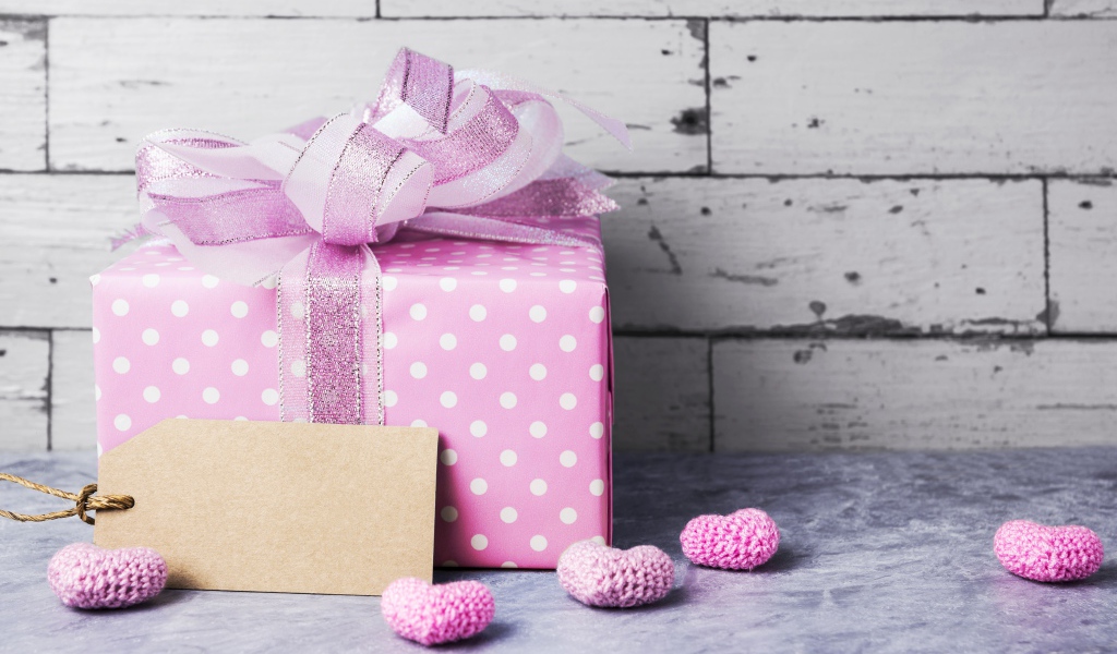 Большая сиреневая подарочная коробка с бантом и маленькими сердечками на фоне стены