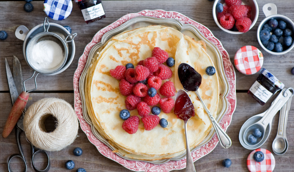 Тонкие блины с малиной и черникой на столе вид сверху