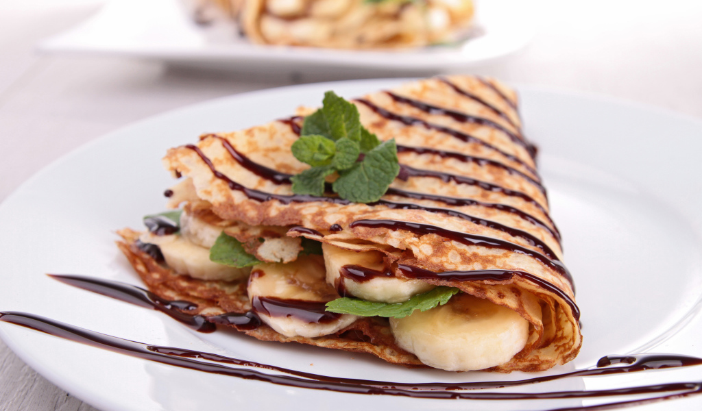 Тонкие сладкие блины с бананами и шоколадом на белой большой тарелке угощение на Масленицу