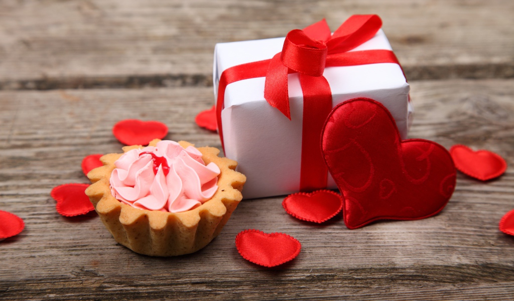 Подарок с красными сердечками и пирожным на столе