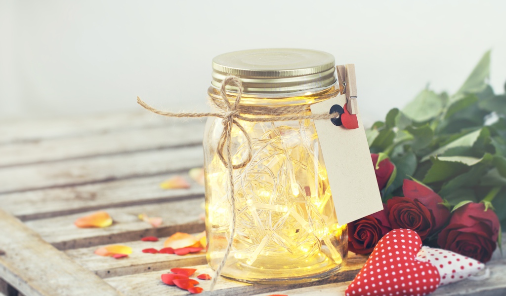 Стеклянная банка с гирляндой на столе с букетом роз и сердечками
