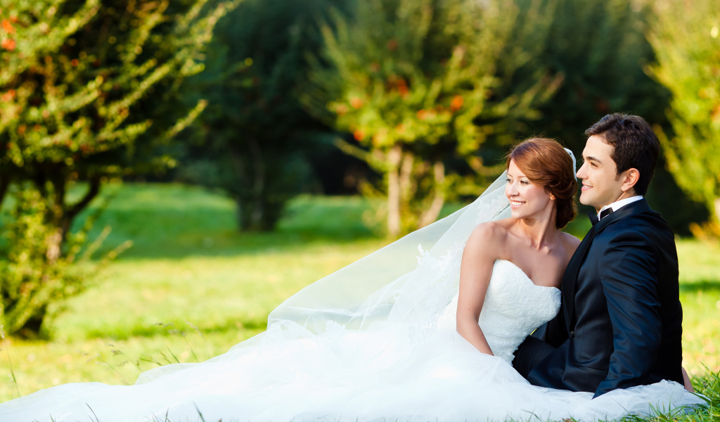 Счастливые жених и невеста сидят на зеленой траве
