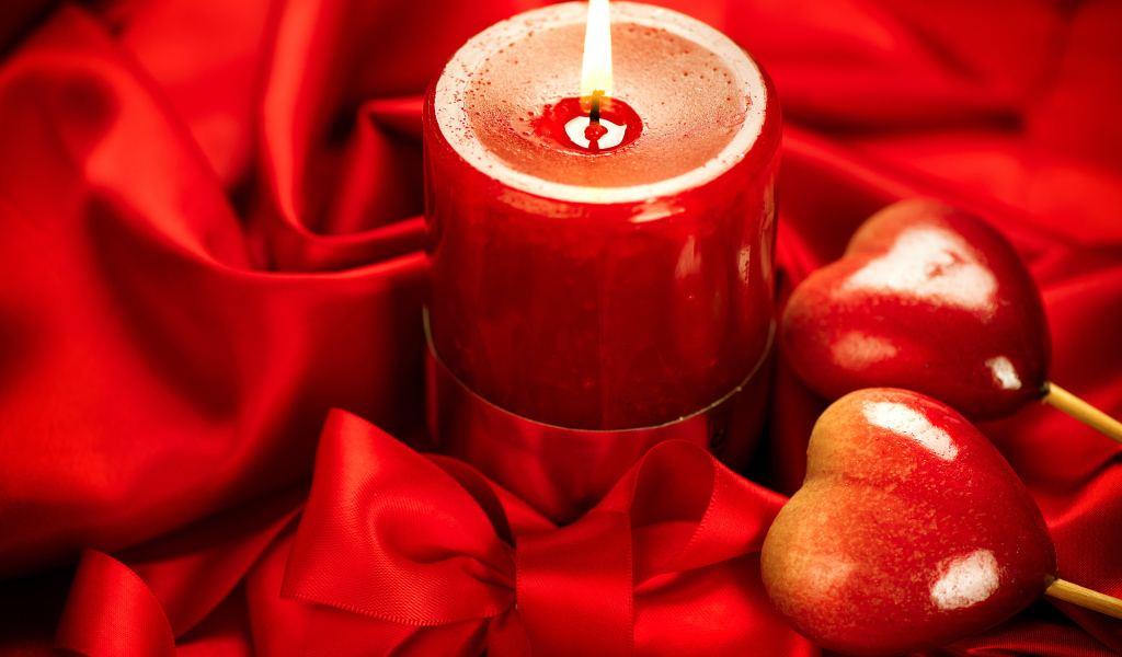 Зажженная свеча с двумя сердечками на красном фоне с бантом