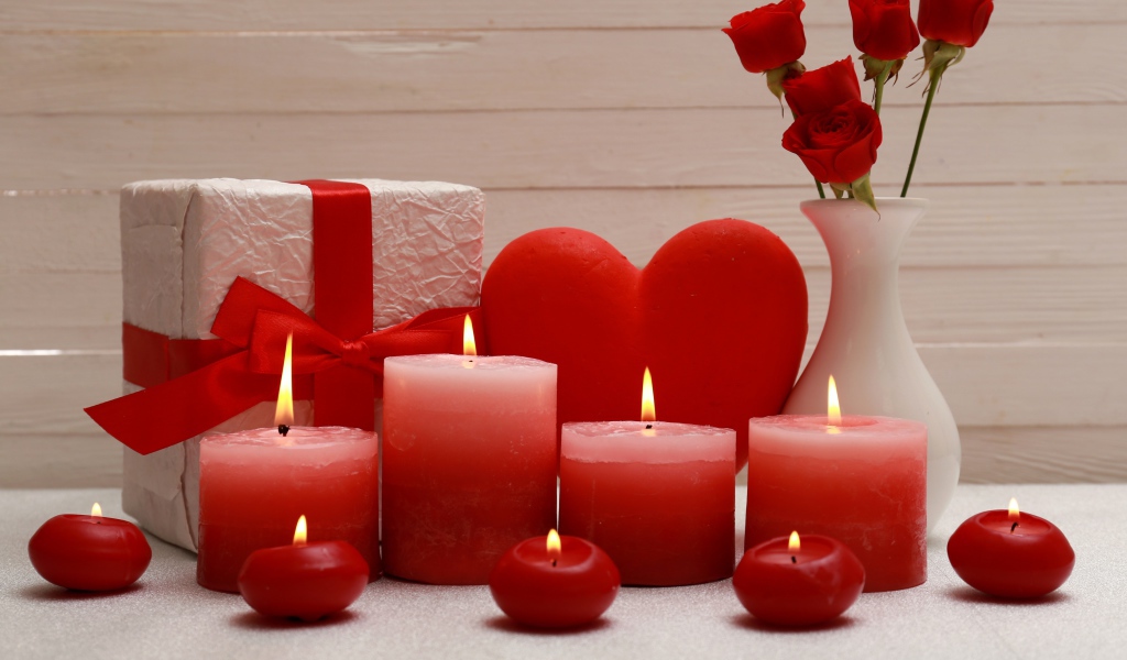 Зажженные красные свечи на столе с подарком, красным сердцем и цветами в вазе 