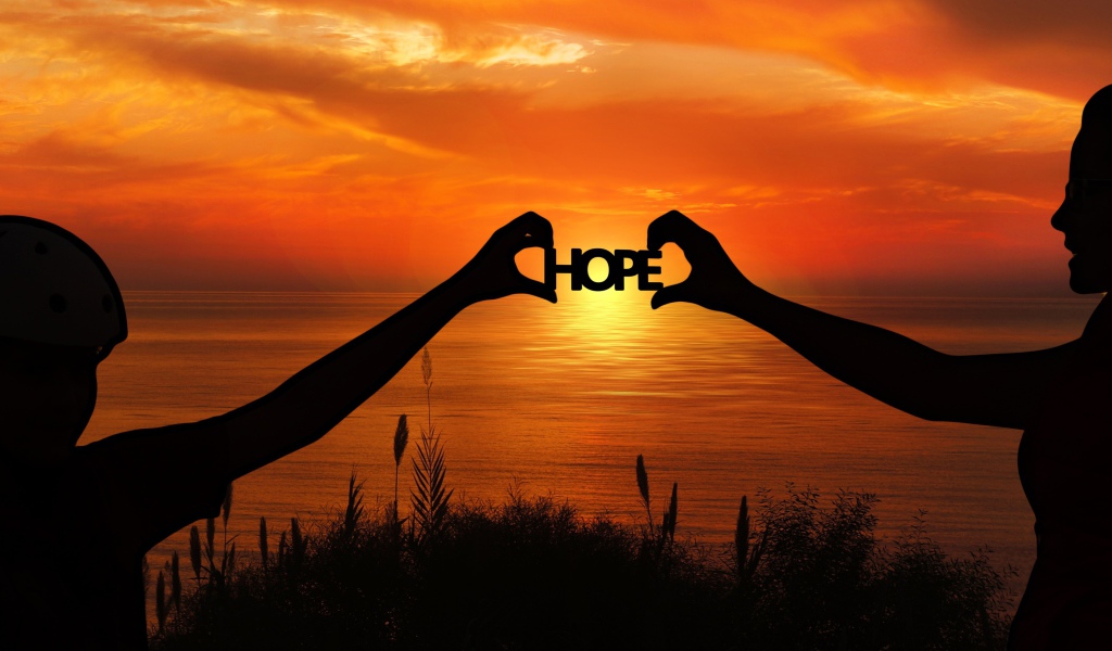 Силуэты пары держат в руках надпись HOPE на фоне заката