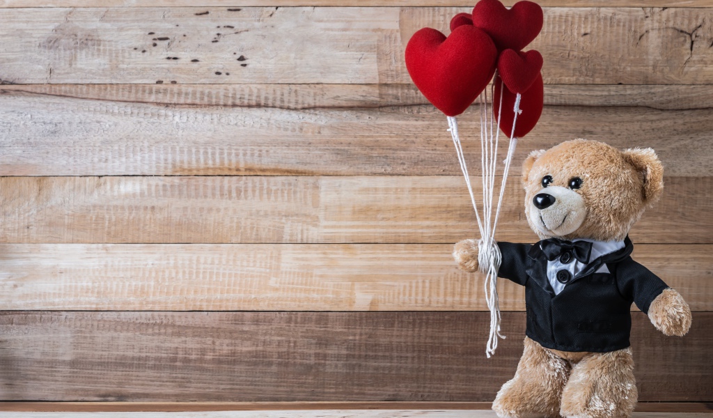 Плюшевый медведь с сердечками на деревянном фоне