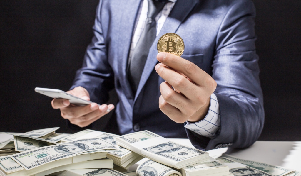 Мужчина с пачками долларов и монетой биткоин в руке