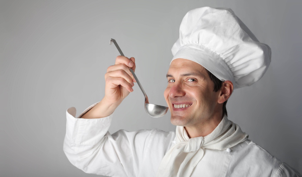 Улыбающийся мужчина повар с половником в руках на сером фоне