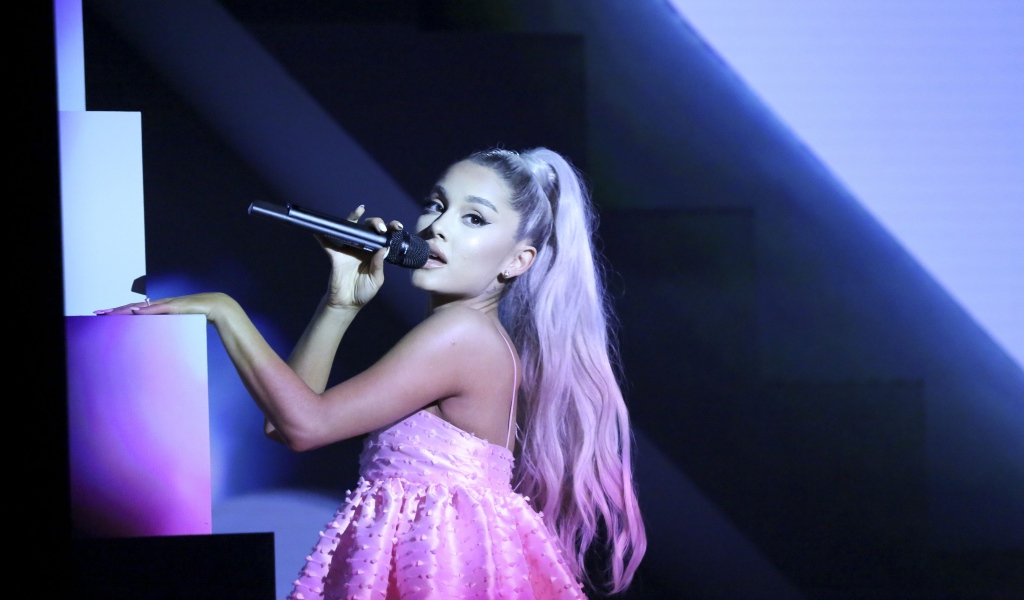 Певица Ариана Гранде на сцене с микрофоном в розовом платье