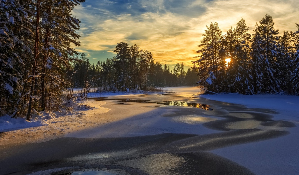 Покрытая льдом река с заснеженными елями по берегам на рассвете
