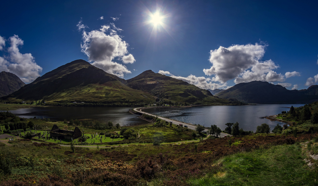 Яркое солнце в голубом небе над горами у реки