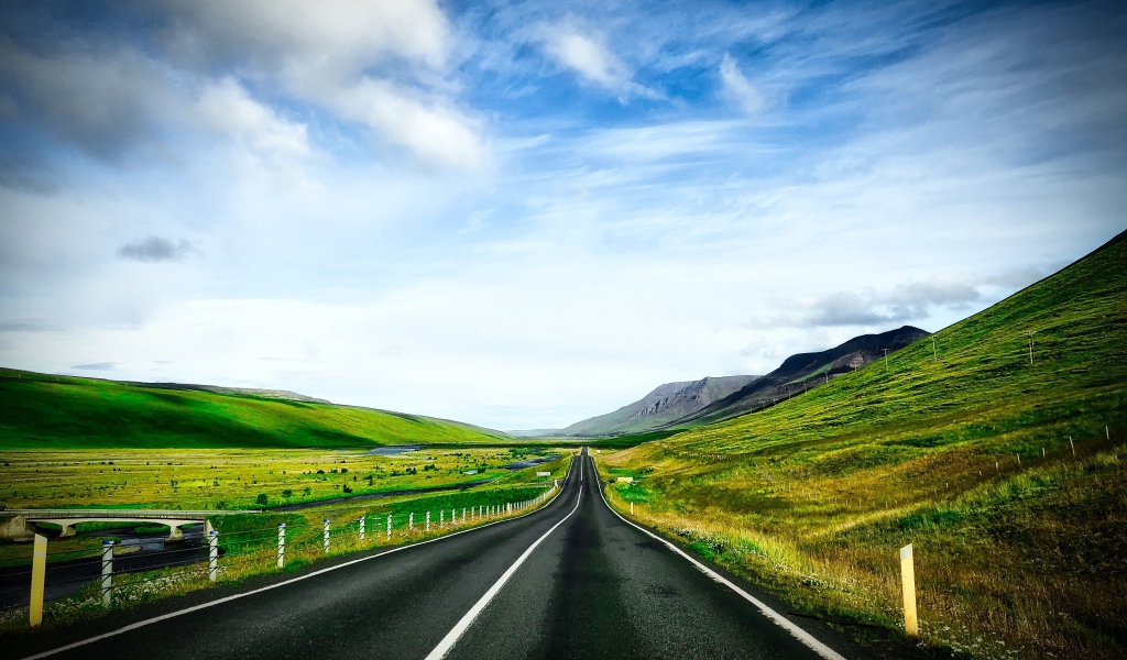 Ровная дорога у зеленых холмов на фоне голубого неба