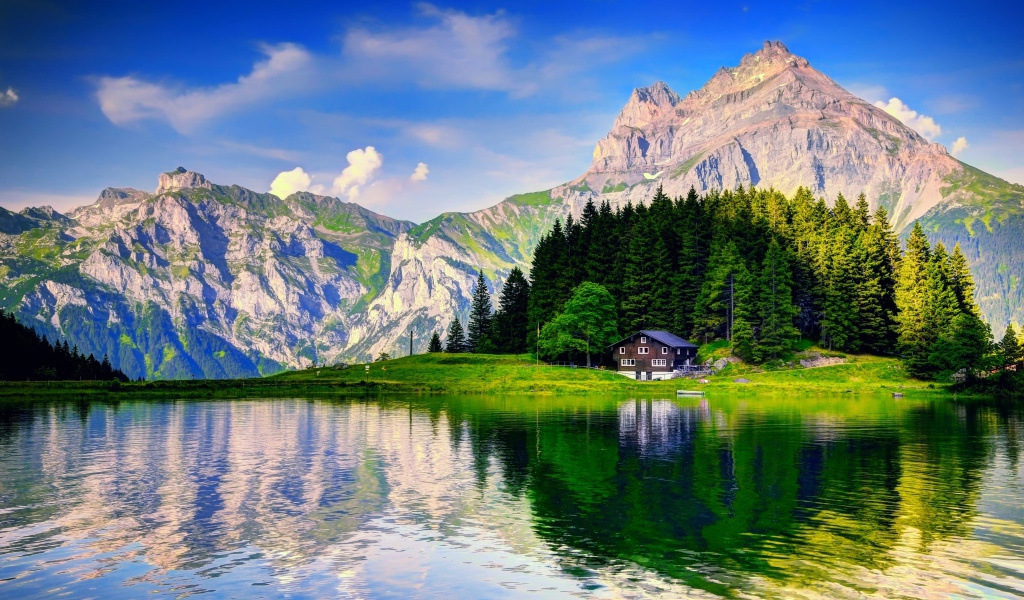 Forest and mountains are reflected in the lake under a beautiful blue sky with white clouds