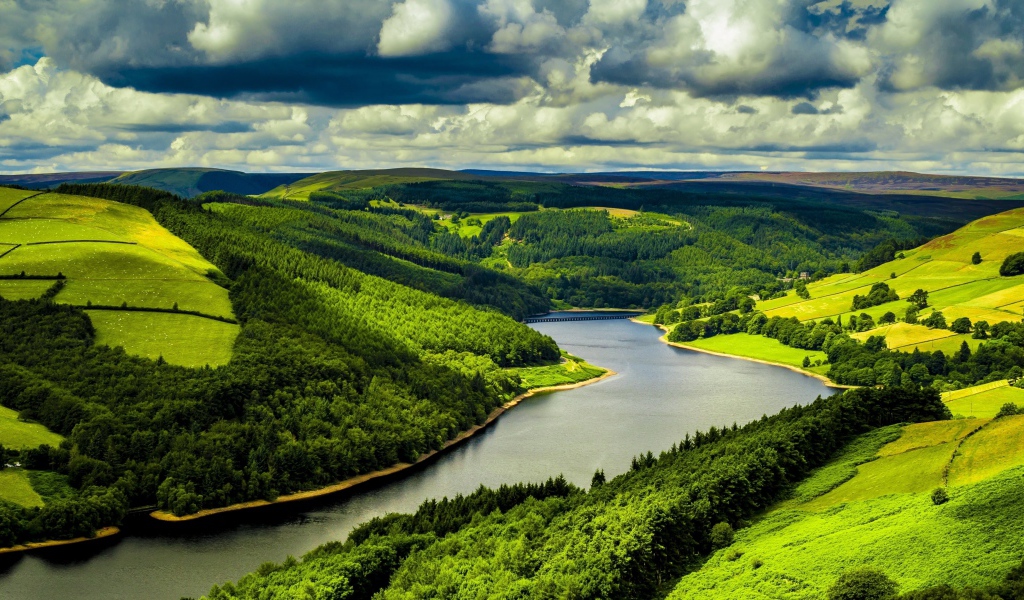 Зеленые холмы у реки под небом с густыми белыми облаками