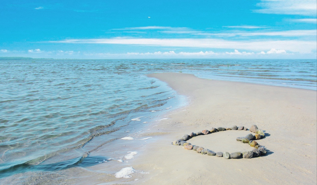 Сердце из камней на песке у спокойного моря под голубым небом