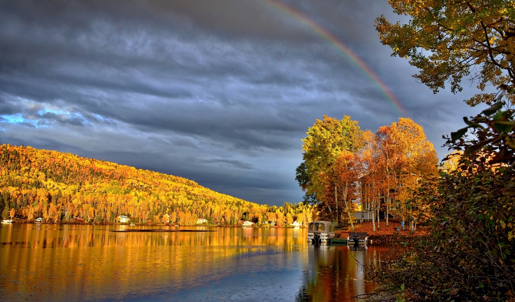 Радуга в пасмурном небе над озером у осеннего леса