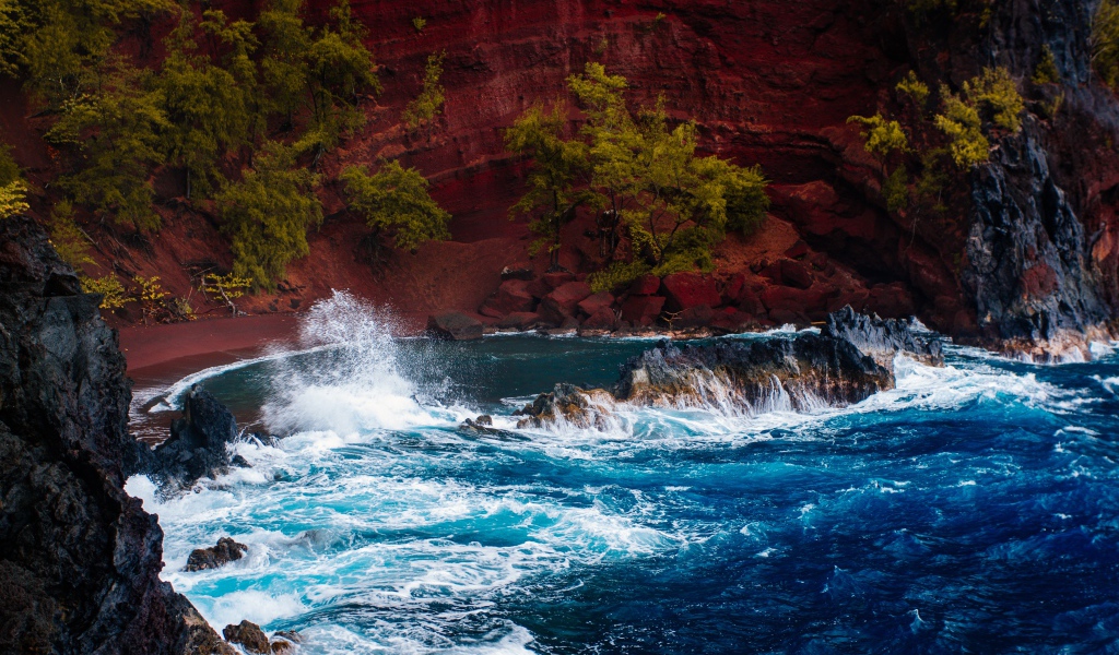 Грубое море брызгает камнями перед красным песчаным океанским заливом в Хане