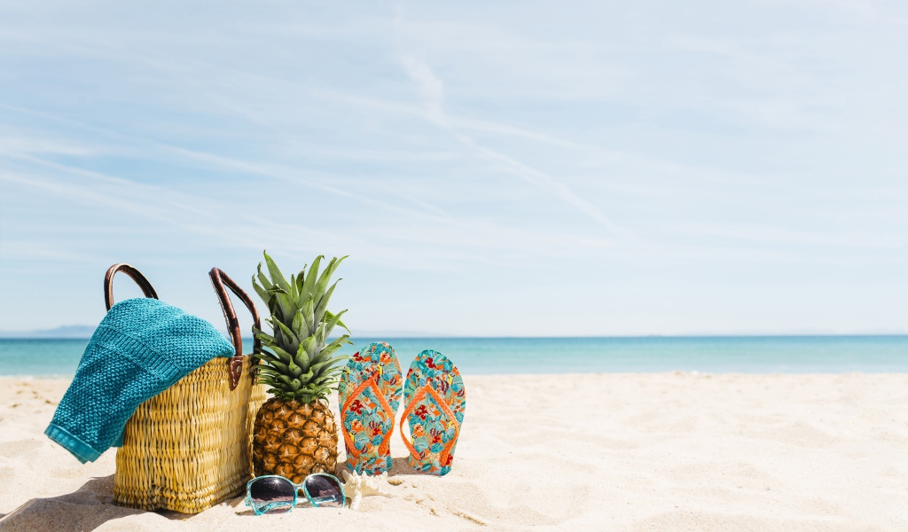 Сумка, ананас, шлепанцы и солнечные очки лежат на песке на пляже летом