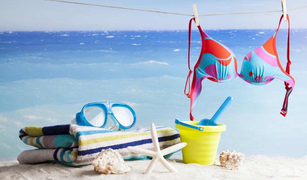 Очки, купальник, полотенце, ракушки и игрушки на песке на пляже летом