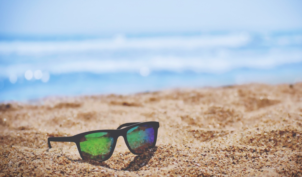 Солнцезащитные очки лежат на желтом песке у моря