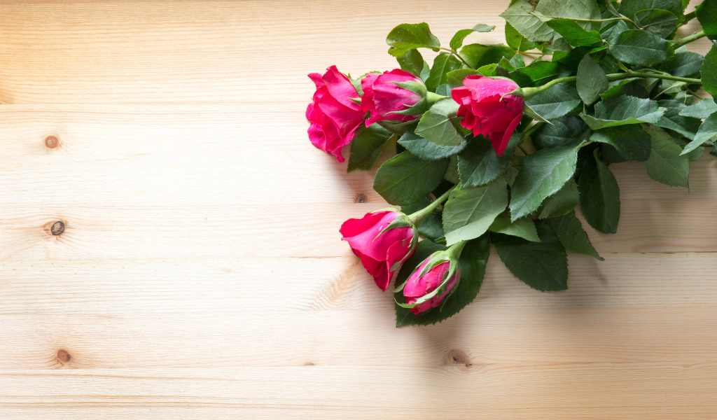 Букет розовых роз с зелеными листьями на деревянной поверхности 