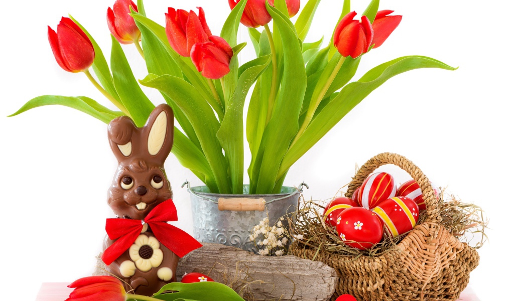 Букет красных тюльпанов на столе с шоколадным кроликом и крашеными яйцами на Пасху