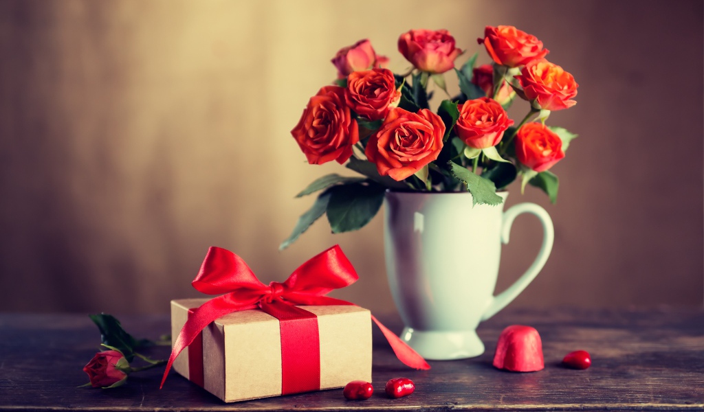 Букет роз в белой вазе с подарком на столе