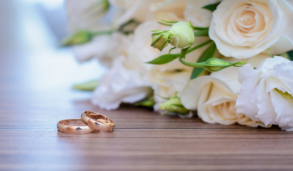 Букет белых роз на столе с золотыми обручальными кольцами