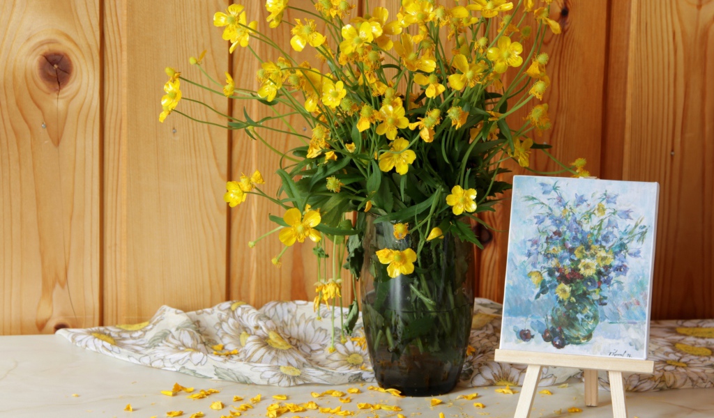 Букет желтых полевых лютиков в стеклянной вазе на столе с картиной