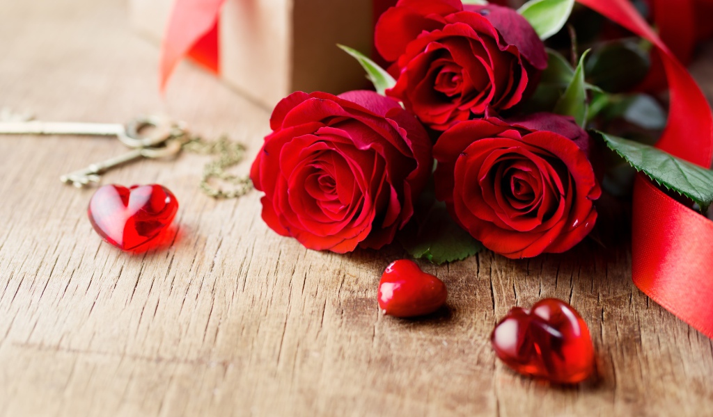 Три красных розы на деревянном столе с красными сердечками