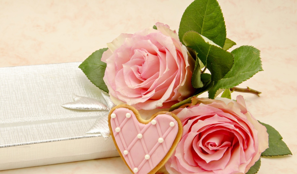 Две розовые розы с печеньем в виде сердца на розовом фоне