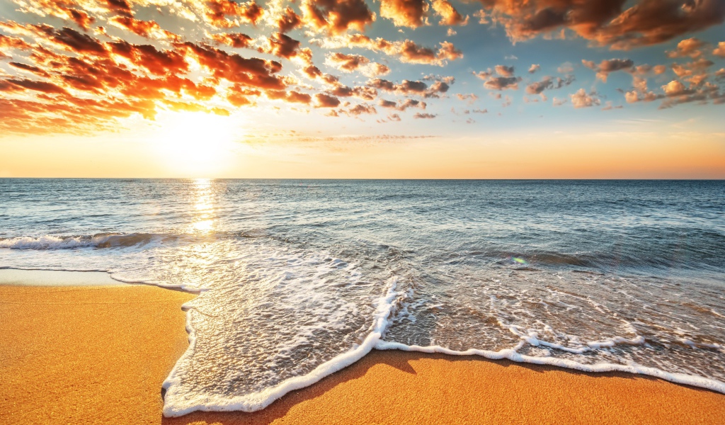 Морская волна омывает песок на берегу под красивым небом