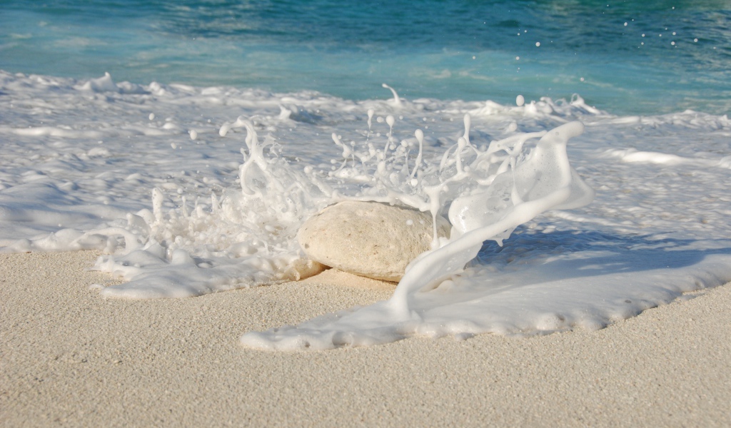 Белые морские волны бьются об камень на желтом песке