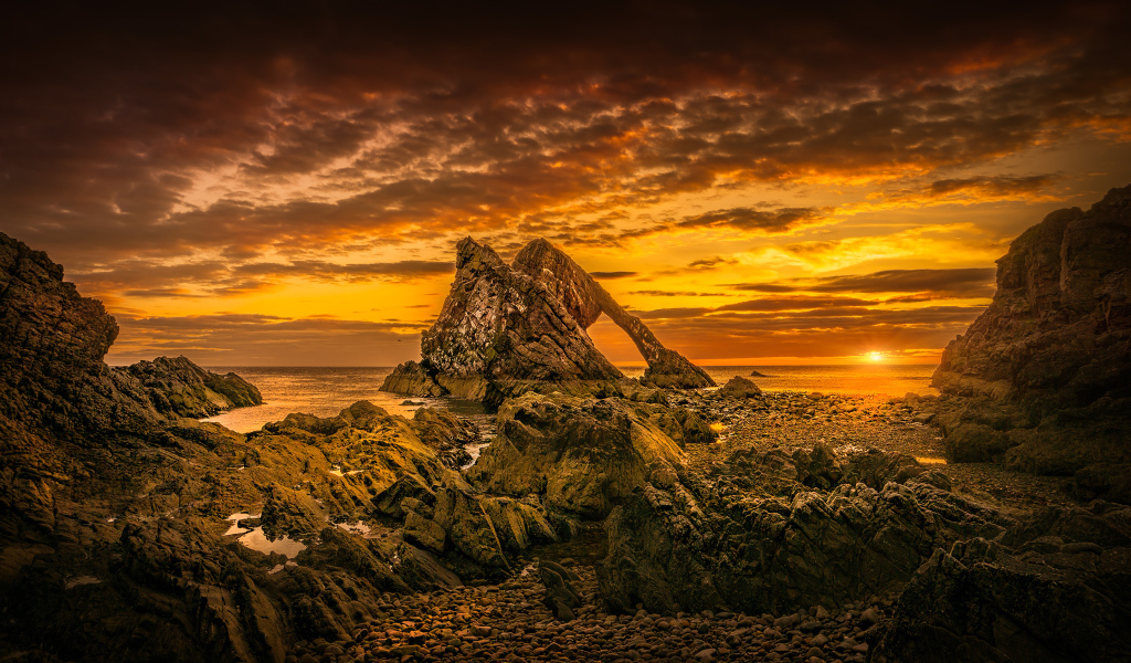 Скала в море на закате солнца под облачным небом