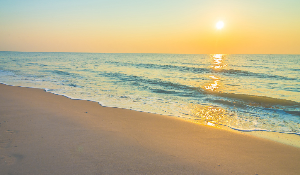 Морские волны на желтом песке на закате солнца летом