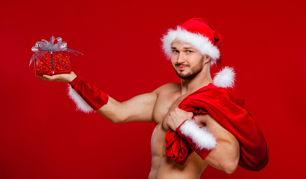 Мужчина в новогоднем костюме Санта Клауса с мешком и подарком в руке на красном фоне