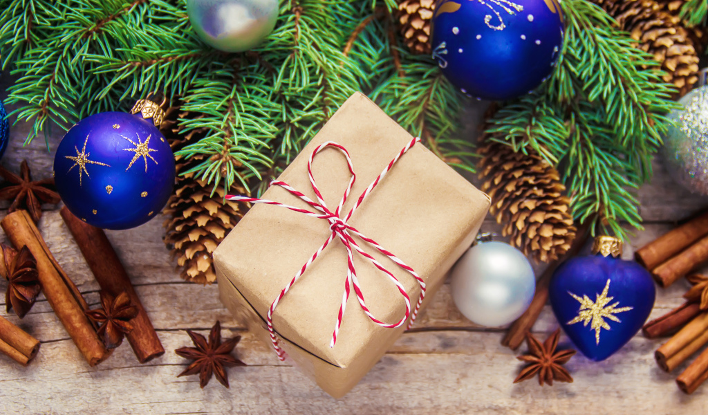 Еловая ветка с игрушками на столе с корицей и подарком на Новый год 