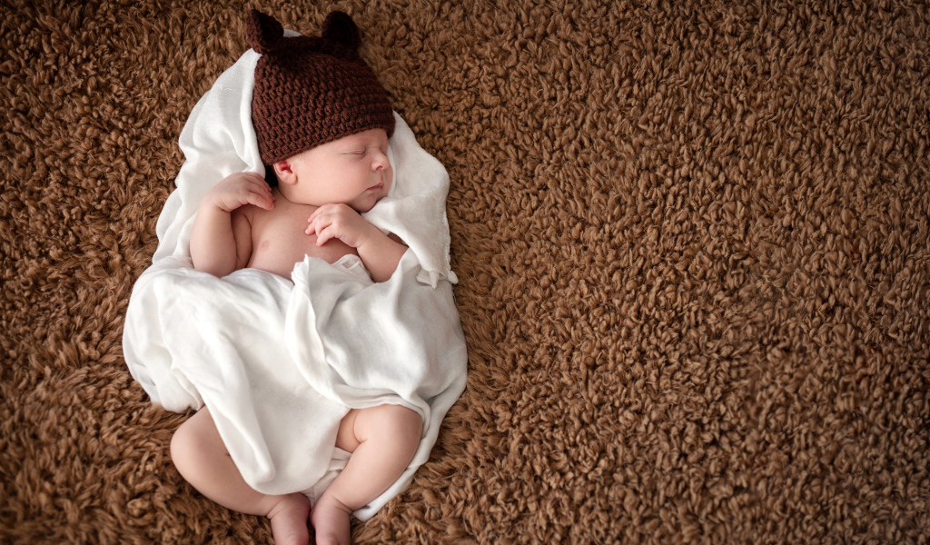 Грудной ребенок в вязаной шапке  спит в белом покрывале 