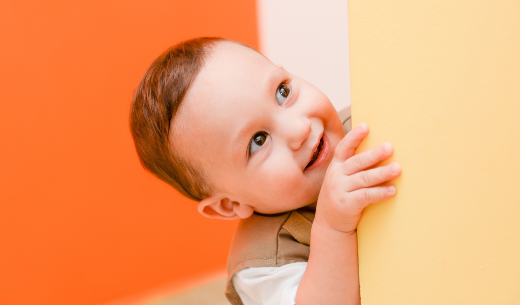 Маленький любопытный мальчик выглядывает из-за стены