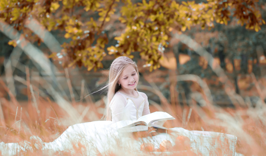 Девочка в красивом белом платье читает книгу на природе